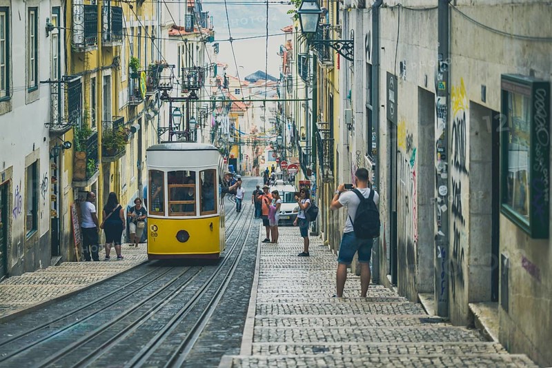A yellow tram descends a steep, narrow alley full of charm in an urban setting, people taking photos, Lisbon, Portugal, Europe
