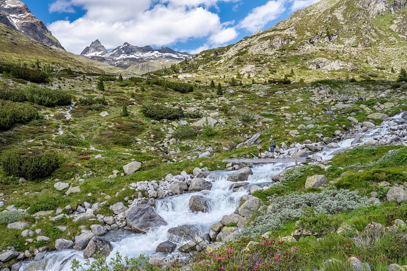 Mountaineer on a bridge over a mountain stream, Hornkeesbach, in front of a picturesque mountain landscape, rocky mountain peaks with snow, Berliner Höhenweg, Zillertal Alps, Tyrol, Austria, Europe