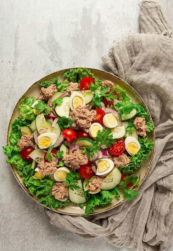 Tuna salad, vegetable salad with quail eggs, lettuce, red onion and cucumbers, on a light gray table, keto food, lifestyle, healthy eating, selective focus, top view, no people