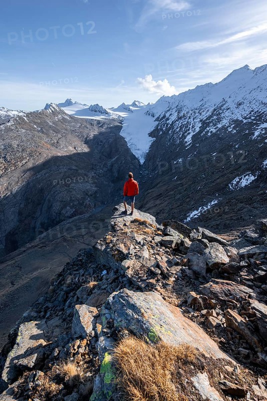 Mountaineer standing on a rock, surrounded by an impressive mountain landscape with snow-covered peaks in autumn View of Gurgler Ferner with summit Hochwilde and Falschungsspitze, Ötztal Alps, Tyrol, Austria, Europe