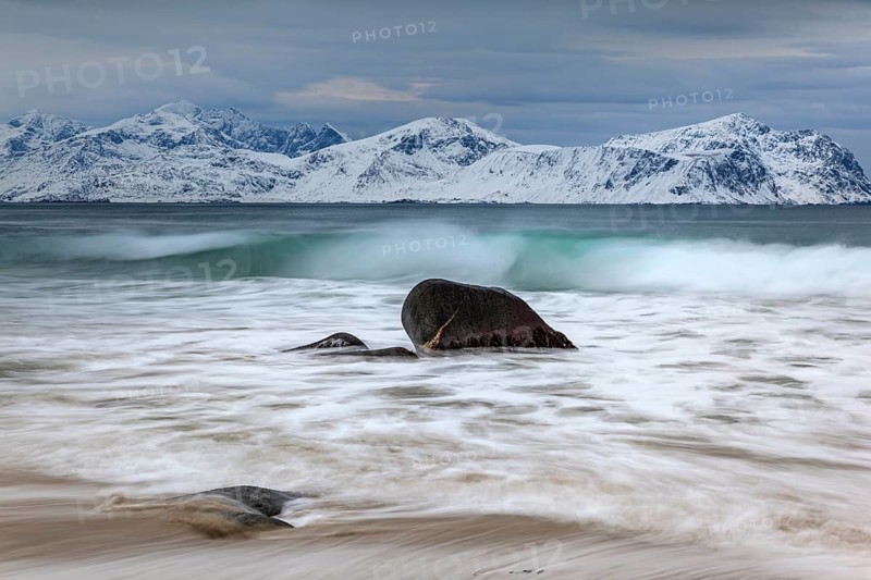 Rocks on the beach in front of snowy mountains, dark clouds, sea, spray, winter, Vikten, Flakstadoya, Lofoten, Norway, Europe