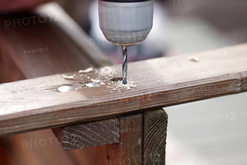 Wood drill, wood shavings, hole, board, DIY, close-up of a cordless screwdriver with wood drill. A hole is drilled in the wood to maintain an old wooden bench