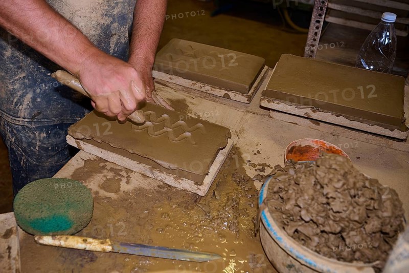 Worker's hand carving patterns in clay bricks, surrounded by clay and tools, Patmos Cotto Brickworks, Traditional Brickmaking, Kampos, Patmos, Dodecanese, Greek Islands, Greece, Europe
