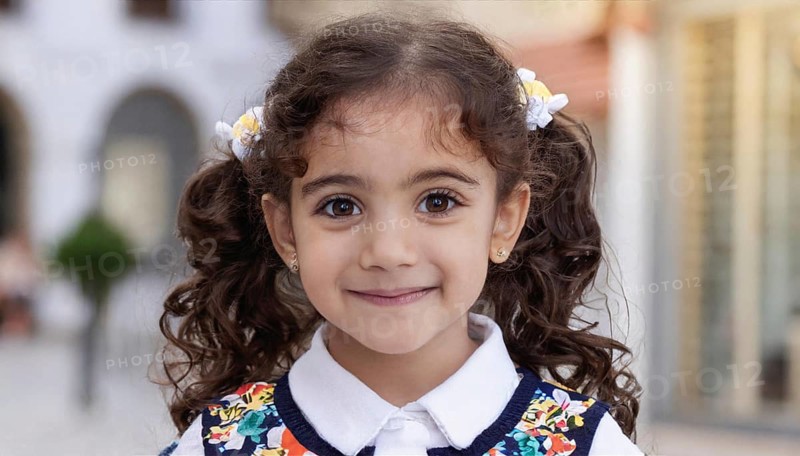 A little girl with pigtails and a floral dress smiles innocently into the camera, showing pure joy and trust, AI generated, AI generated