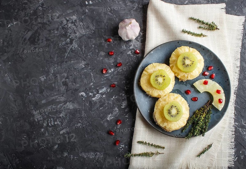 Pieces of baked pork with pineapple, cheese and kiwi on black background, top view, copy space