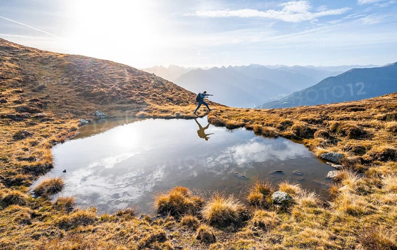 Mountaineer jumping, reflected in a small mountain lake on the Krahberg, mountain panorama in autumn, Venet crossing, Ötztal Alps, Tyrol, Austria, Europe