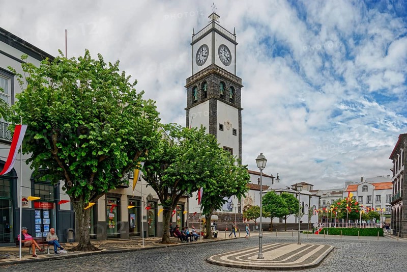 Clock tower towers over trees lining the paved walkway as people stroll, Igreja Matriz de São Sebastião, Ponta Delgada, Sao Miguel Island, Azores, Portugal, Europe