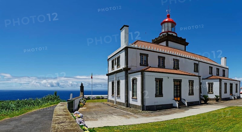 A white lighthouse with red roofs and a display by the sea under a clear blue sky, Farol da Ferraria lighthouse, Sao Miguel Island, Azores, Portugal, Europe