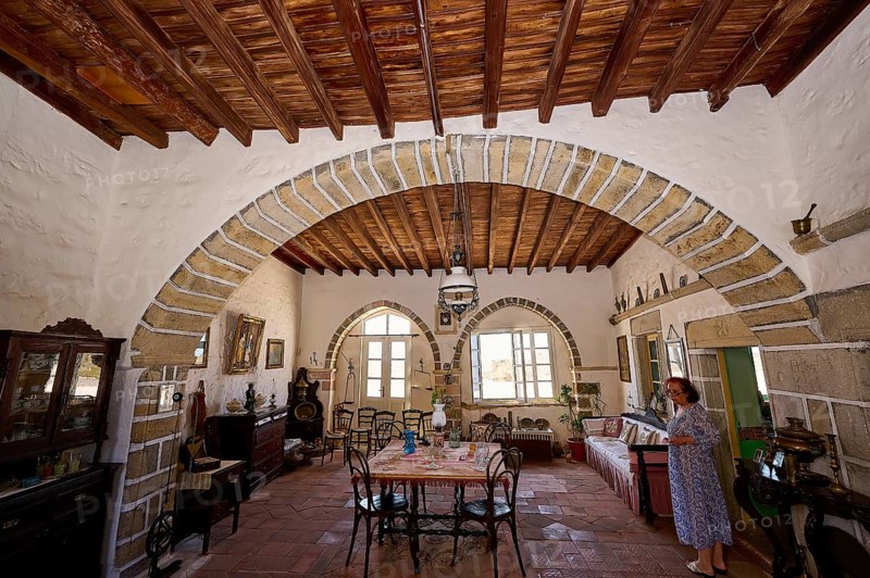 Dining room with round arch, rustic wooden floors, antique furniture and bright natural light. One person can be seen, Simantiris House, Chora, main town Patmos, Patmos, Old Town, Dodecanese, Greek Islands, Greece, Europe