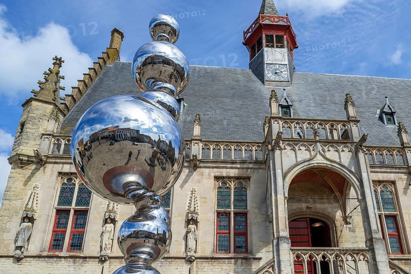 Market square reflected in shiny modern artwork in front of the Brabantine Gothic town hall in the city Damme in summer, West Flanders, Belgium, Europe