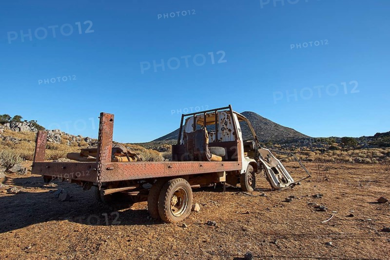 A badly decayed lorry, its loading area exposed, stands in a dry desert landscape under a wide blue sky, Wrecked vehicle, Crete, Greek Islands, Greece, Europe