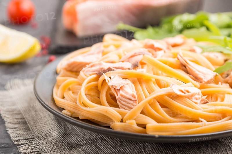 Semolina pasta with salmon and salmon steak on a black concrete background and linen textile. Side view, close up, selective focus