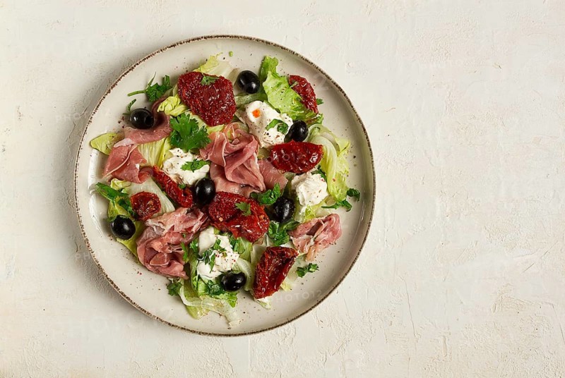 Salad with dried tomatoes, prosciutto, soft cheese, olives, homemade, top view