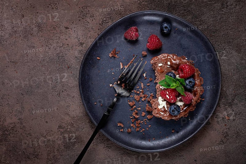 Half-eaten chocolate tartlet, on a plate, stuffed with cottage cheese and berries, breakfast, homemade, no people