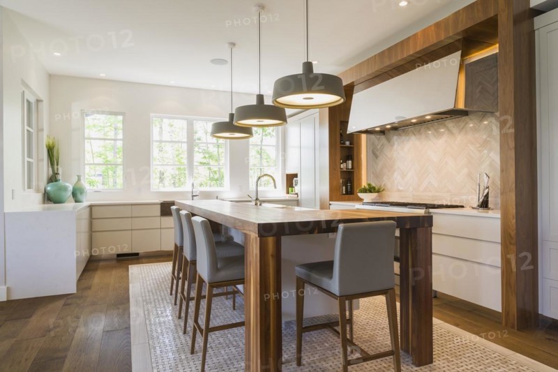Walnut wood island with grey leather and wooden high chairs on travertine mosaic floor surrounded by engineered hickory wood floorboards in kitchen inside a luxurious contemporary bungalow style home, Quebec, Canada, North America