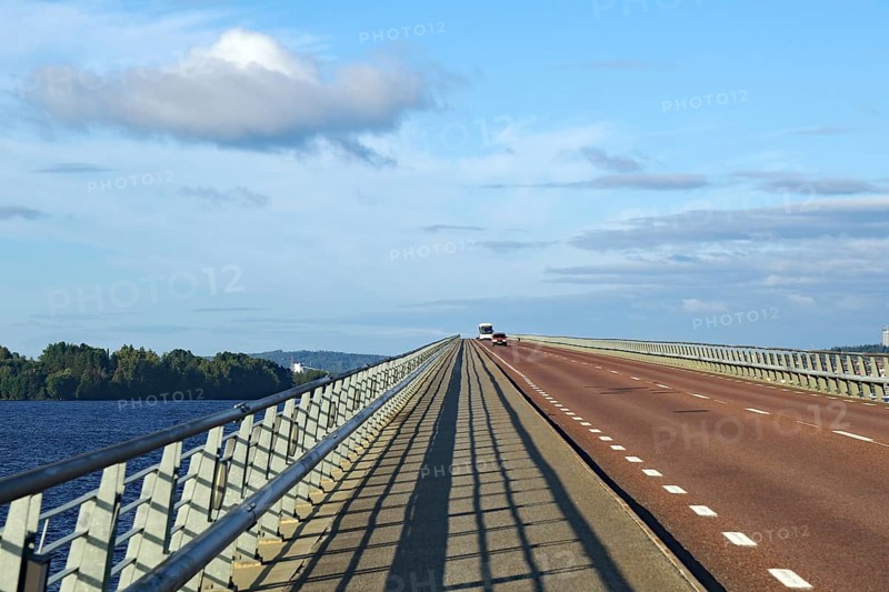 Long bridge over water with blue sky and few clouds, shadow on road, Storsjon, Fröson Bridge, Östersund, Jämtland, Sweden, Europe