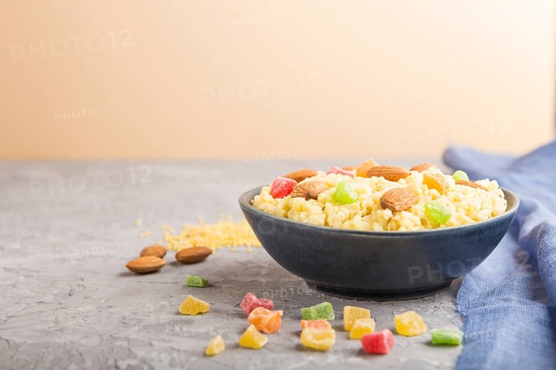 Millet porridge with candied fruits and almonds in blue ceramic bowl on a gray and orange background and blue linen textile. Side view, close up, selective focus, copy space