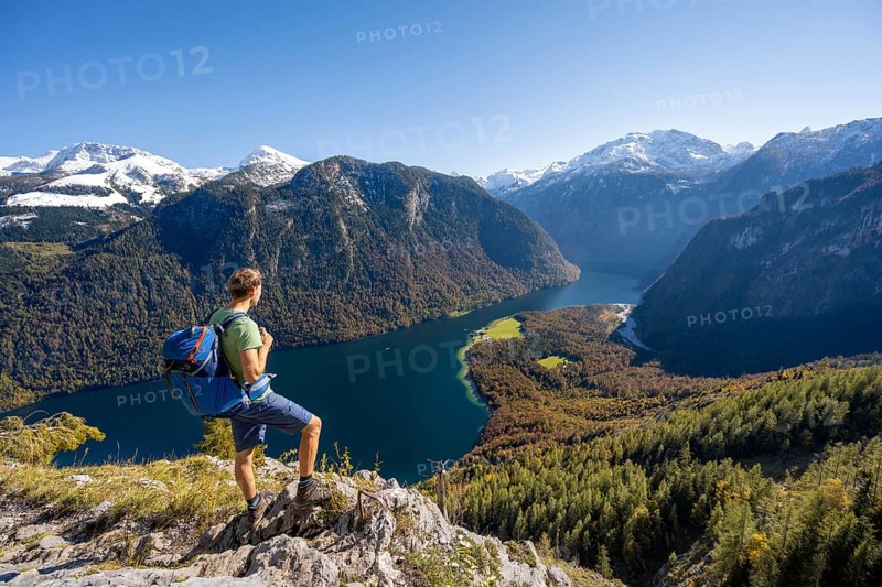 Mountaineer on an exposed mountain hiking trail, Rinnkendlsteig, view of the Königssee, autumnal forest and yellow larches with snow-covered mountains, Berchtesgaden National Park, Berchtesgadener Land, Upper Bavaria, Bavaria, Germany, Europe