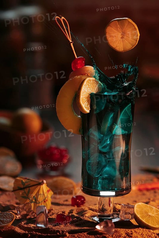 Sparkling cocktail in a glass with ice cube cubes, decorated with lime slices and cherries on a sandy background in a sunset atmosphere