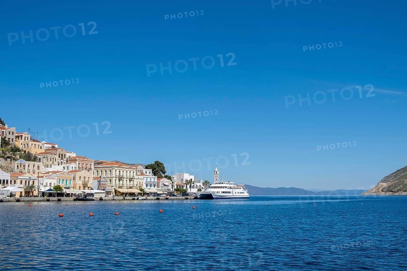 A picturesque coastal town with white houses and a boat in the clear blue sea under a bright blue sky, Symi Island, Dodecanese, Greek Islands, Greece, Europe