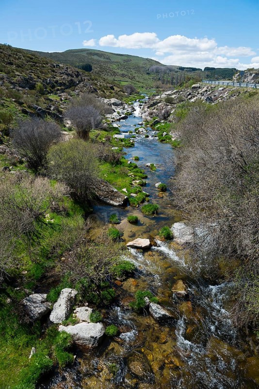 River with rocks and vegetation in a green valley under a blue sky with clouds and mountains, Garganta de Navarenas O Arenillas, Navarenas Gorge, Sierra de Gredos, Ávila, Avila, Madrid, Spain, Europe