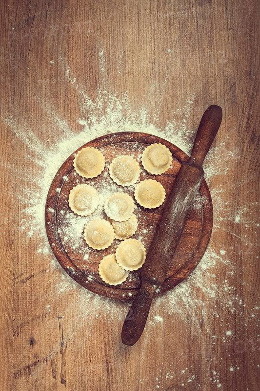 Fresh raw, uncooked ravioli, on a cutting board, with a rolling pin for dough, wooden background, no people