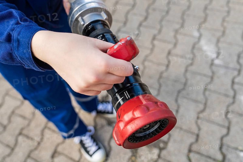 Child holding a fire hose with red handles on a cobbled floor, fire brigade, Enzklösterle, Black Forest, Germany, Europe