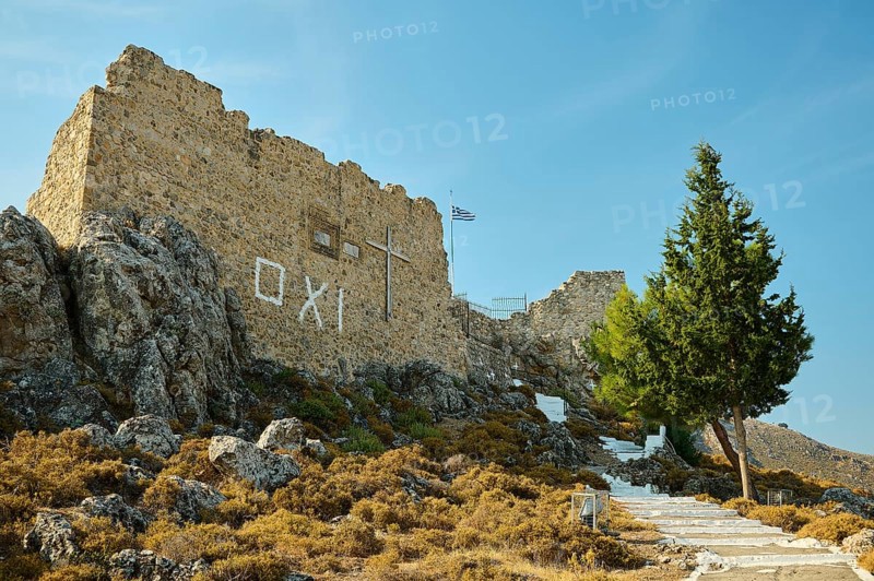 Stone ruin with cross on a hill, stairway and Greek flag under a clear sky, St John's Castle, Oxi Graffiti, Archengelos village, Rhodes, Dodecanese, Greek Islands, Greece, Europe