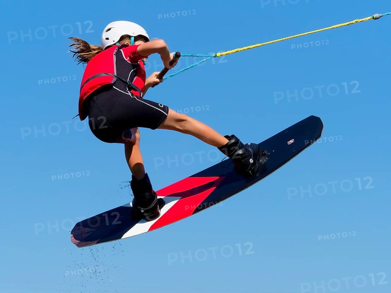 Boy or girl, jump over jump with wakeboard, red life jacket and water sports, water skiing in the wake park
