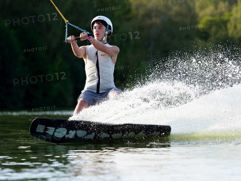 Sporty young man with helmet and waistcoat on wakeboard in lake, water sports, water skiing in wakepark