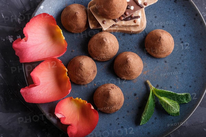 Chocolate truffle on blue ceramic plate on black concrete background decorated with rose petals. close up, top view
