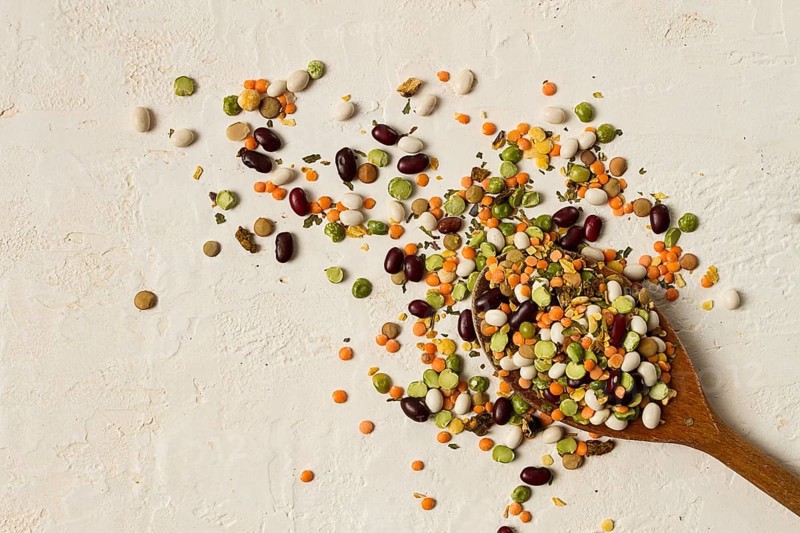 Wooden spoon, with an assortment of legumes, beans, peas, top view, on a light background