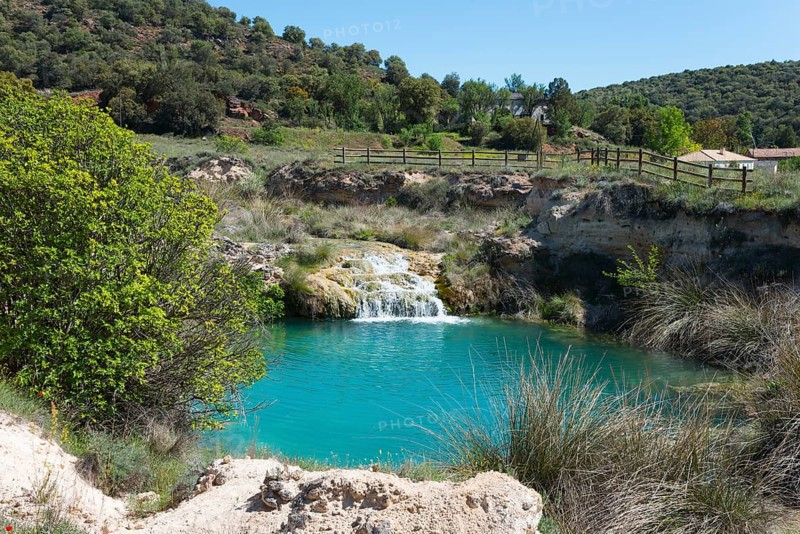 A small waterfall plunges into a turquoise-coloured lake, surrounded by dense meadows and hilly landscape, Lagunas de Ruidera National Park, Albacete province, Castilla-La Mancha, Spain, Europe