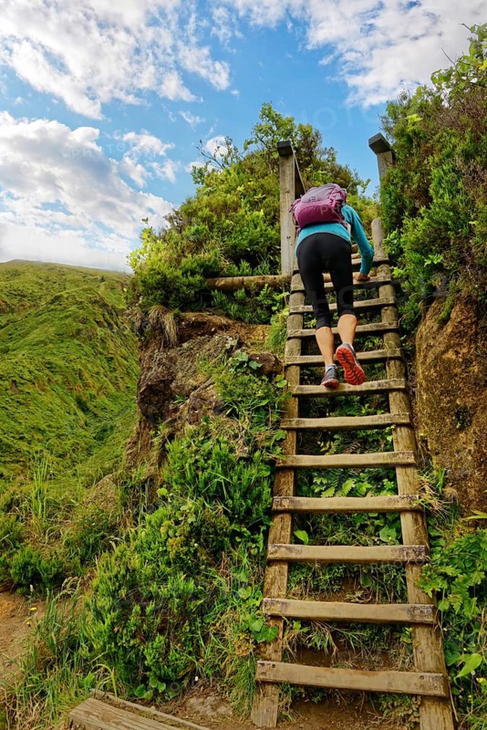 Person climbing up a wooden staircase surrounded by green vegetation, clear sky and clouds, crater lake Lagoa do Fogo, Caldeiras, Sao Miguel Island, Azores, Portugal, Europe