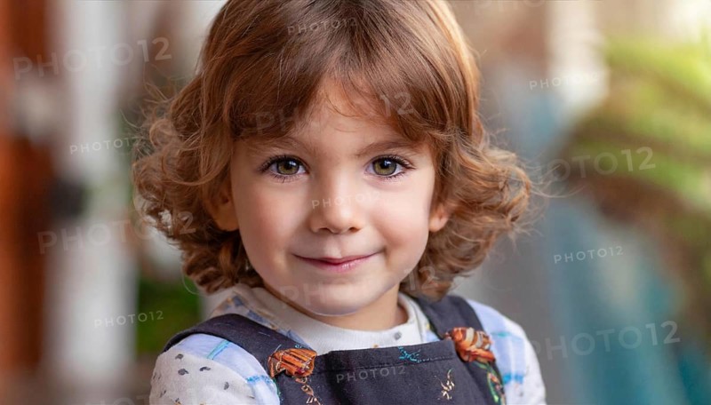 A smiling girl with curly hair wears dungarees and a polka-dot shirt, plants can be seen in the background, AI generated, AI generated