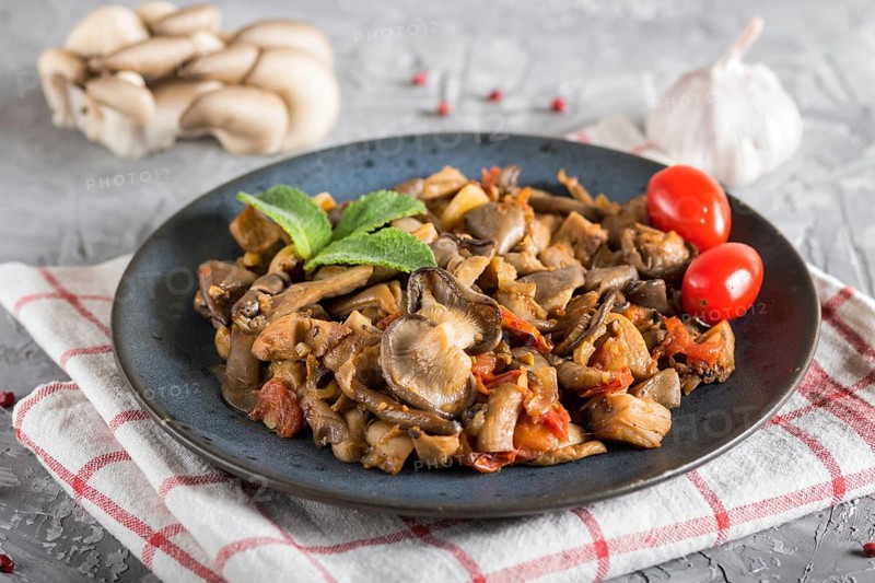 Fried oyster mushrooms with tomatoes on gray concrete background. side view, close up