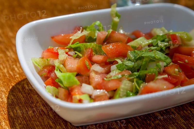 Close-up of a fresh salad with tomatoes, onions and green leaves in a white ceramic bowl on a wooden surface, Turkey, Asia