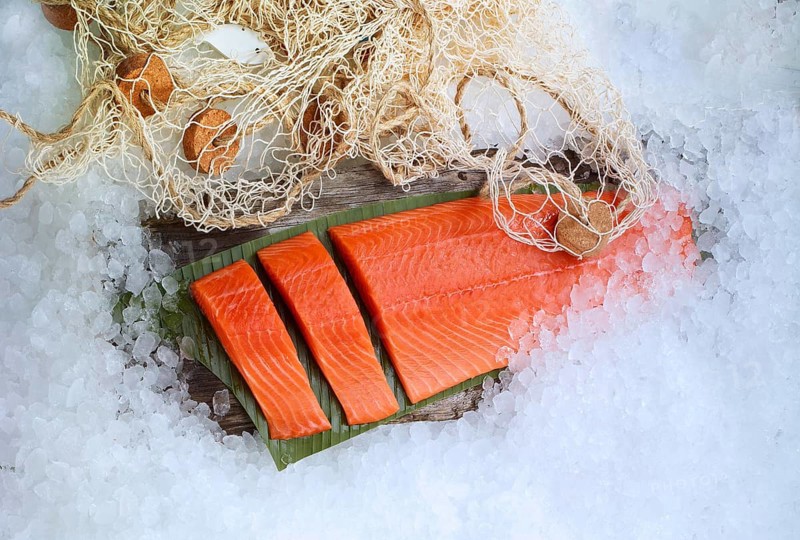Salmon (Salmo) lying on a banana leaf and lots of ice, fishing net as decoration, studio shot