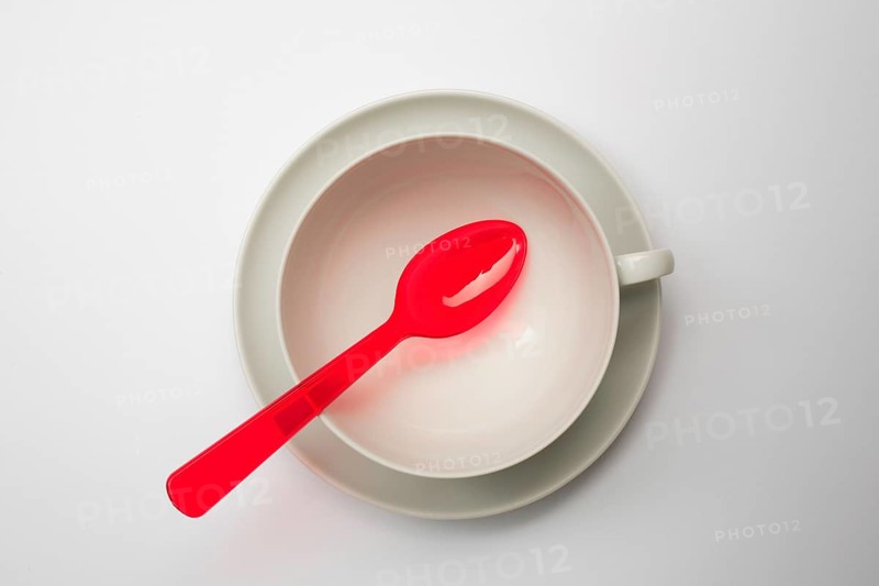 Crockery and cutlery, empty teacup with saucer, seen from above, a red plastic spoon lies on it