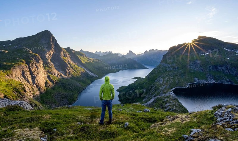 Mountaineer looking over mountain landscape with pointed mountain peaks and fjord Forsfjorden with village Vindstad, sun star at sunrise, Moskenesøya, Lofoten, Nordland, Norway, Europe