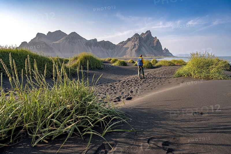 Tourist on a sand dune, Black beach with volcanic sand, Sand beach, Dunes with grass, Stokksnes headland, Klifatindur mountain range, Austurland, East Iceland, Iceland, Europe