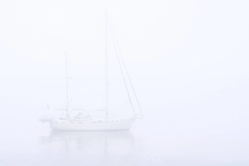 Sailboat, sailing boat, yacht with lowered sails anchored at sea during bad visibility due to thick fog, dense mist