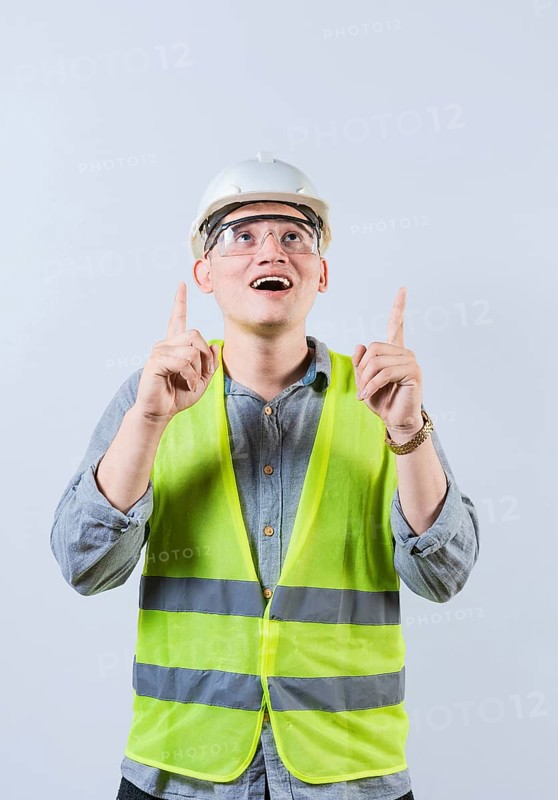 Surprised young architect pointing up. Amazed engineer pointing at an advertisement. Engineer with astonished face pointing at blank space