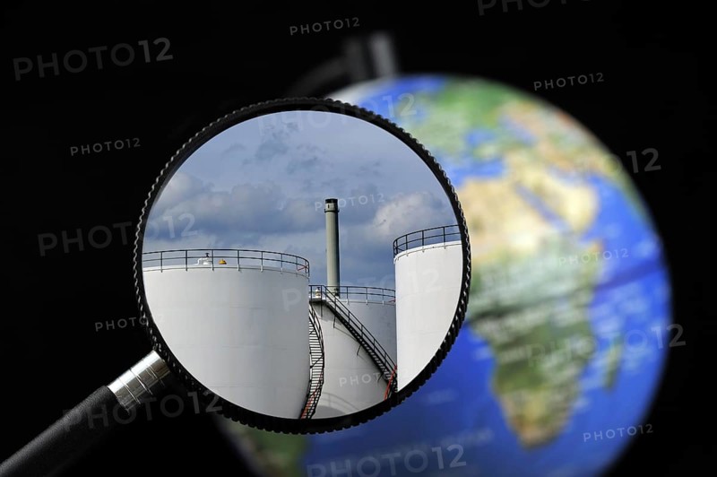 Storage tanks of oil refinery from the petrochemical industry seen through magnifying glass held against illuminated terrestrial globe