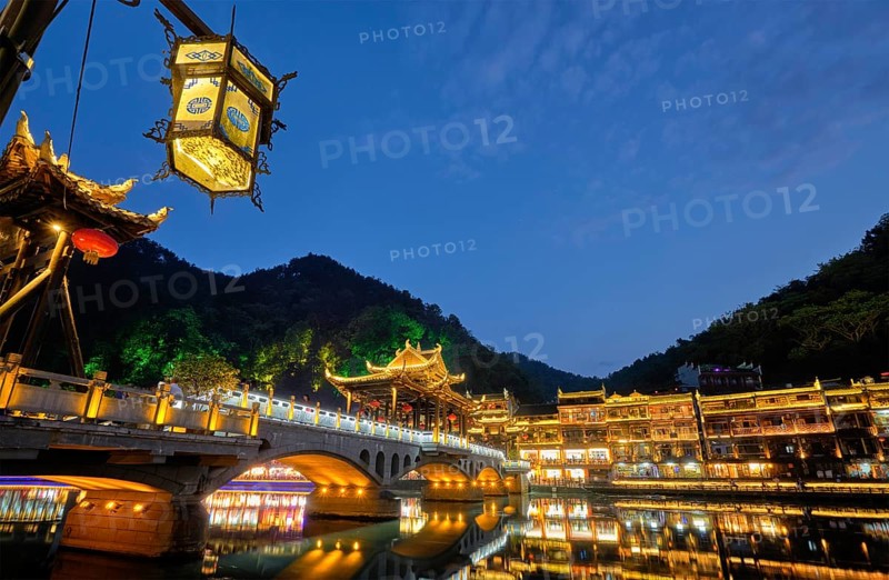 Chinese tourist attraction destination, Feng Huang Ancient Town (Phoenix Ancient Town) on Tuo Jiang River with bridge illuminated at night. Hunan Province, China, Asia