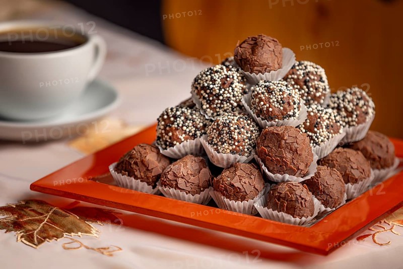 Close-up of rum balls with chocolate on a plate and a coffee cup in the background