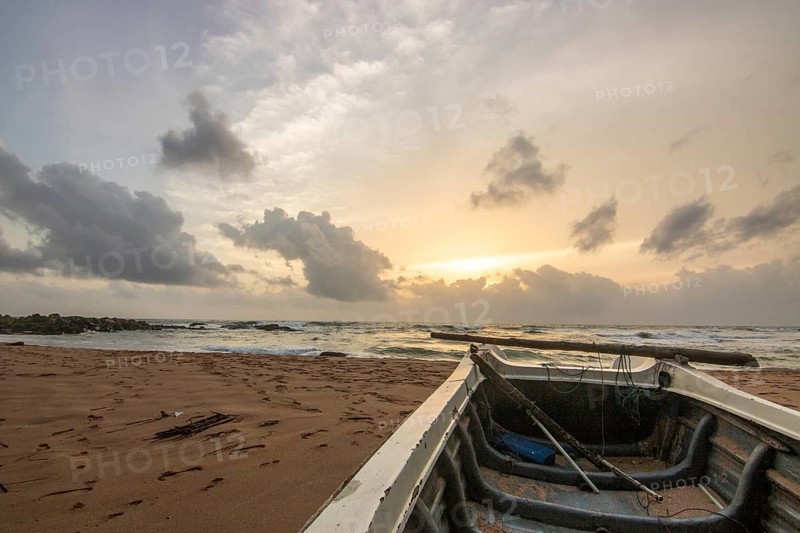 Landscape by the sea and sandy beach. A boat lies in the sand and adds a special touch to the picture at sunset. Storm in Bentota, Sri Lanka, Asia