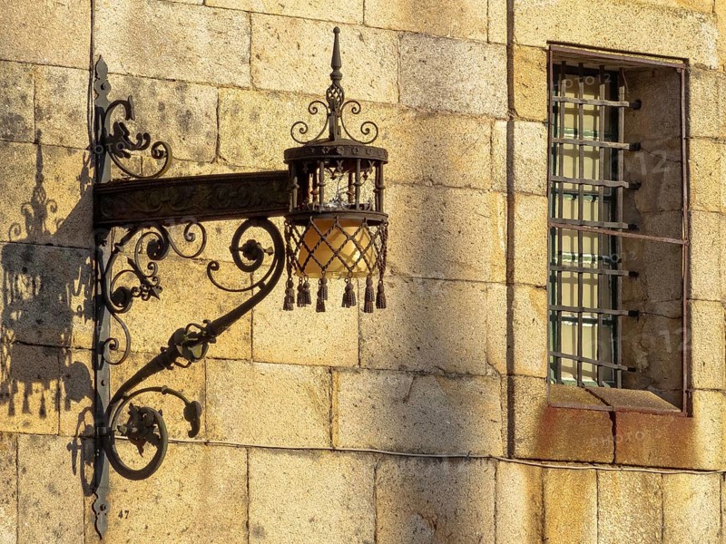Old wrought iron lamp and window with security bars on the stark wall of the Convent of San Paio de Antealtares on the Quintana Square (Praza), Santiago de Compostela, Galicia, Spain, Europe