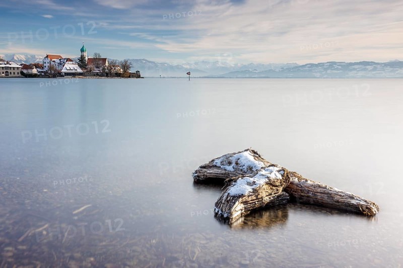 Wooden trunk and picturesque church of St George on the lakeshore in front of snow-covered Pfänder on a clear winter's day, moated castle, Lake Constance, Bavaria, Germany, Europe