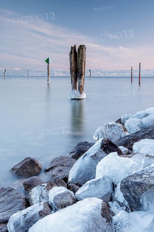 A wooden pile and ice-covered stones on a calm body of water under a blue sky in winter, harbour, Immenstaad, Lake Constance, Baden-Württemberg, Germany, Europe